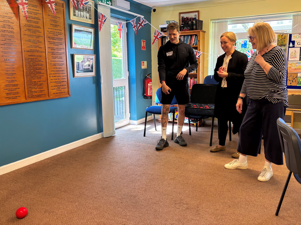 A young man, dressed in sportswear, showing two women how to play the sport of boccia.