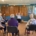 A group of people aged 70+ sat with their hands in the air doing seated exercising