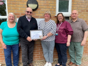 5 people standing outside a village hall holding a certificate
