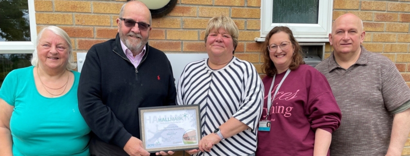 5 people standing outside a village hall holding a certificate