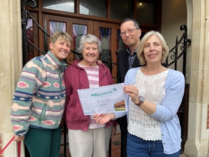Four trustees standing outside a village hall holding a certificate