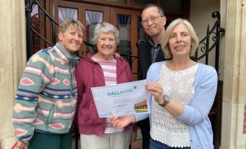 Four trustees standing outside a village hall holding a certificate