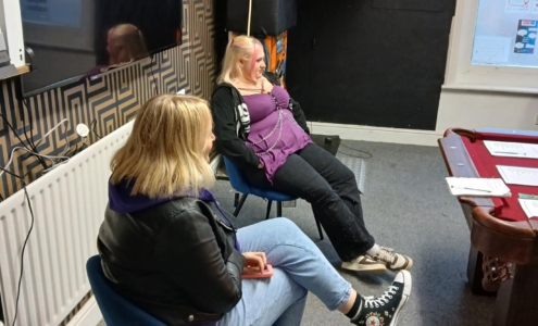 two teenage girls with blond hair sat under a TV and looking at a snooker table