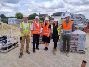 five people in high vis jackets and hard hats posing outside a rural affordable housing development site